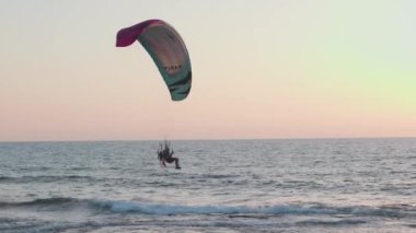 Yamaç paraşütü denizin üzerinde uçar ve keskin bir dönüş yapar. Gökyüzündeki Paraalan bulutların ve günbatımının arka planına karşı. Gökyüzünde paragliding.