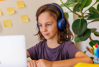 Çocuk derste müzik dinler. Kıvırcık saçlı çocuk mesafeli öğrenme ile mutlu. Dersler İnternet üzerinden yapılıyor.
