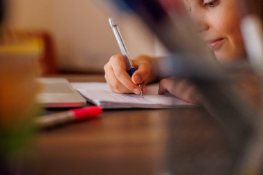 Çocuk eli, yakın plan. Çocuk mektup yazmak için bir kurşun kalem kullanıyor. Çocuk bir deftere yazmayı öğreniyor. anaokulu eğitimi konsepti.