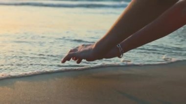 Dişi eller gün batımında deniz dalgalarına dokunur. Eller yukarı. Gün batımında deniz. Sakin ve meditasyon konsepti.