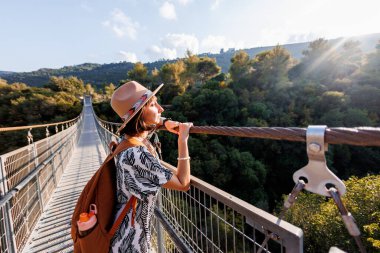 Şapkalı genç kız asma köprüde duruyor ve hayallerindeki uzaklığa bakıyor. yakın plan.