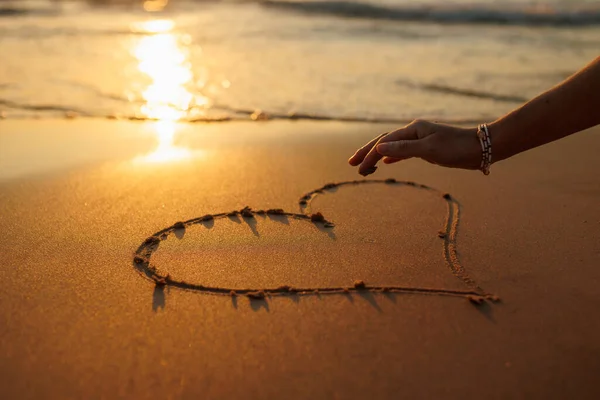 Women's hands draw a heart on the sand. love and relationships. walk on the beach at sunset.