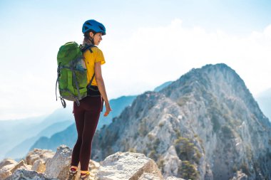 Sırt çantası ve kasklı kadın tırmanışçı yaz günü tırmanmadan önce muhteşem dağ manzarasının tadını çıkarıyor. macera ve dağcılık kavramı. 