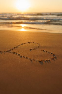 Gün batımında kumsalda bir kalp çizilir. Sahilde romantik bir gün batımı. Kalp şeklinde. Kalp sembolü. Aşk.