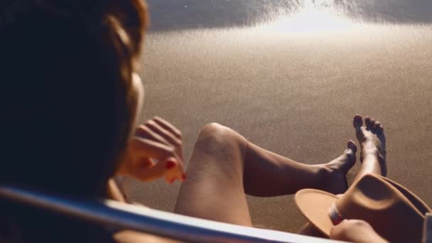 夏のビーチホリデーコンセプト 彼女の手で帽子で太陽のラウンジャーでリラックスしている若い女の子 — ストック動画