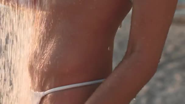 美丽的年轻女子在靠近大海的海滩上洗澡 迷人的年轻女子穿着白色泳衣 在游泳后的日落时享受着阵雨 在海上度假 — 图库视频影像
