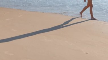Güzel bir kız gün batımında bikinisiyle sahilde yürüyor, tatili boyunca deniz ve güneşin tadını çıkarıyor. Bacaklarını kapat..