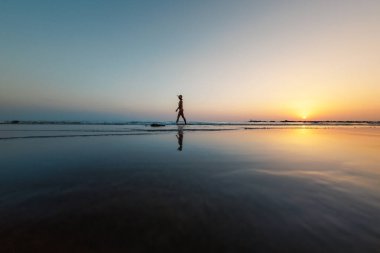 Deniz kıyısında yürüyen bir kadının silueti. Ruhani Barış Meditasyonu. Mutlu bir kız gün batımının arka planında deniz kenarında yürüyor. yan görünüm.