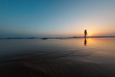 Deniz kıyısında yürüyen bir kadının silueti. Ruhani Barış Meditasyonu. Mutlu bir kız gün batımının arka planında deniz kenarında yürüyor. yan görünüm.