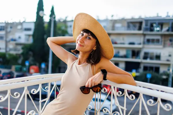 young girl is standing on the balcony. portrait of a beautiful girl in a hat on a balcony in the city. vacation in the city.