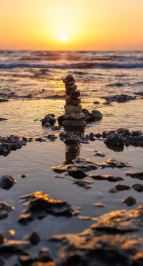 Gün batımında sahilde taş dengesi. Sahildeki küçük çakıl taşlarının piramidi. Taşlar, gün batımında deniz kıyısının arka planında.