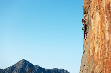 Bir kadın kayaya tırmanıyor. Doğal arazide eğitim. Olağanüstü bir spor. Dağcı doğal bir rahatlama ile antrenman yapar. İpli genç bir kadın kayaya tırmanma sporu için içeri girer..
