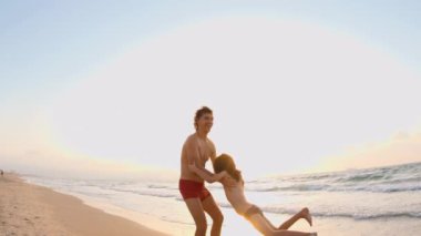 Mutlu baba ve oğul sahilde birlikte oynuyorlar. Baba oğlunu döndürüyor, ellerini tutuyor. Dertsiz, mutlu, neşeli yaşam tarzı.