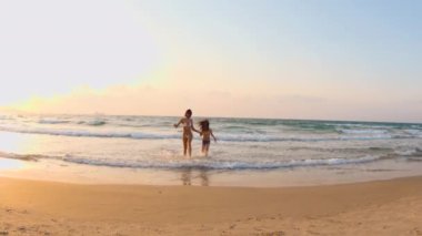 Mutlu genç anne ve oğlu kumsalda kumsalda koşuyor, gülümsüyor ve birlikte eğleniyorlar. Aile deniz tatili.