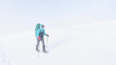 Sırt çantalı bir kadın karda kar ayakkabılarıyla yürüyor, kış yürüyüşü, kışın dağlarda macera, yürüyüş ekipmanları..