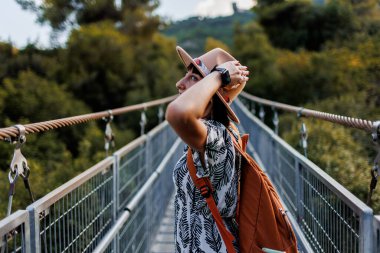 Şapkalı kız asma köprü boyunca yürüyor. Açık havada sonbahar sezonu, asma köprüde yürüyen bir kadının portresi. seyahat ve macera.