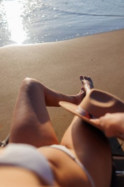 Yaz plajı tatili konsepti. Genç kız elinde şapkasıyla güneşlenirken dinleniyor. bacaklar kapalı.