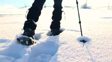 Bir kadın karda kar ayakkabılarıyla yürür, kış yürüyüşü yapar, kışın dağlarda yürüyüş malzemesi taşır.