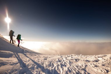 Kar fırtınası sırasında kar ayakkabıları ve sırt çantalı iki kız karda yürür. Büyük dağlarda dağcılık.