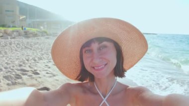 Kız selfie çekiyor. Sahilde selfie çeken, yaz şapkalı neşeli bir genç kızın yakın çekimi. Sahilde tatil..