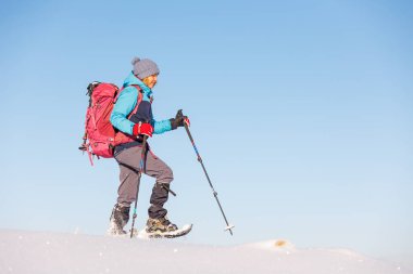 Dağlara tırmanan. Sırt çantalı ve kar ayakkabılı bir kız karda yürüyor. Dağlarda kış yürüyüşü.