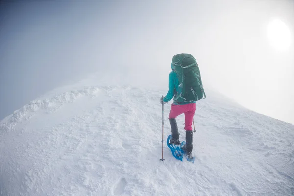 Climber in the mountains. A girl with a backpack and snowshoes walks through the snow. Winter trekking in the mountains.