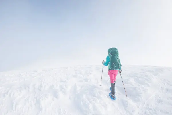 Climber in the mountains. A girl with a backpack and snowshoes walks through the snow. Winter trekking in the mountains.