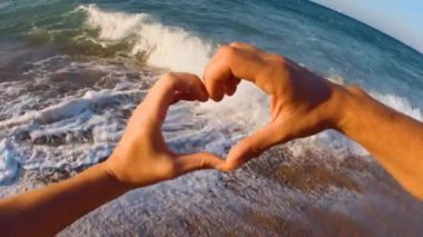 Denizin arka planında kalp şeklinde elleri olan genç ve mutlu bir çift var. Aşk ve delicesine aşık olma kavramı.