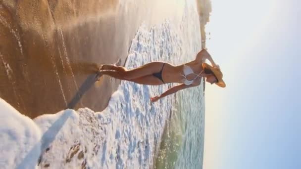 垂直射击 日落时分 穿着帽子和泳衣的快乐的小女孩沿着海滩散步 在海上度假 海岸上美丽的夕阳 — 图库视频影像