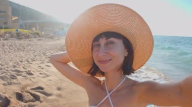 Kız selfie çekiyor. Sahilde selfie çeken, yaz şapkalı neşeli bir genç kızın yakın çekimi. Sahilde tatil..