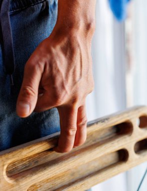 Kaya tırmanışçısının güçlü erkek eli, parmak eğitimi için bir tahta tutuyor. tırmanma egzersizi. Kaya tırmanışçısının eli yakın çekim. Güç ve dayanıklılık. Klavye ve askı. ekstrem spor