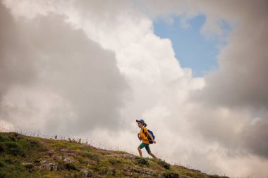 Çocuk sırt çantasıyla dağlardaki bulutların arkasına gidiyor. Sırt çantalı çocuk gezgini, yürüyüş, seyahat, yaşam tarzı konsepti