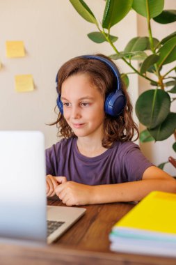 Çocuk derste müzik dinler. Kıvırcık saçlı çocuk mesafeli öğrenme ile mutlu. Dersler İnternet üzerinden yapılıyor.