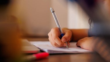 Çocuk eli, yakın plan. Çocuk mektup yazmak için bir kurşun kalem kullanıyor. Çocuk bir deftere yazmayı öğreniyor. anaokulu eğitimi konsepti.