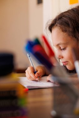 Evde masasında otururken ödevini yaparken yazmayı öğrenen odaklanmış küçük bir çocuğun yan görüntüsü. Yazmayı öğrenen zeki bir anaokulu öğrencisinin portresi.. 