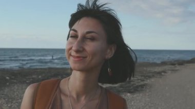 Güzel, doğal, güzel bir kadın gülümseyip gülüyor, kumsalda kameraya poz veriyor. Kumsalda gülümseyen ve mutlu bir kızın portresi..