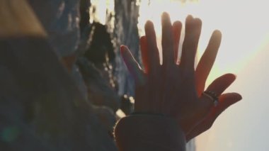 Dikey çekim. Kız gün batımında deniz kıyısında dururken ellerini ve parmaklarını gösteriyor. Sakin ve meditasyon konsepti.