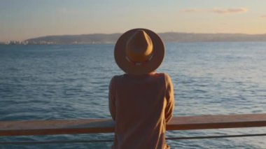 Paltolu ve şapkalı şık ve güzel bir kadın denize bakıyor. Sur boyunca yürü. Denize yakın bir sonbahar. sakinlik ve sükunet.