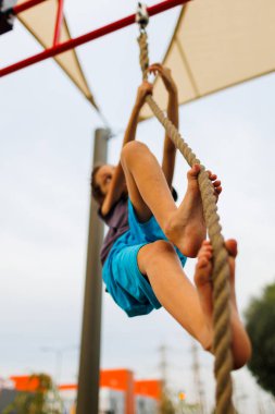 Çocuk eğitimi. Güçlü bir çocuk ipe tırmanır. Çocuk spor sahasında antrenman yapıyor. Çocuk spora gider.