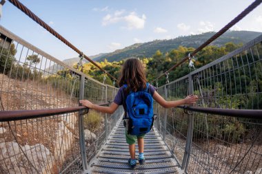 Sırt çantalı çocuk kanyonu ip köprüsünden geçiyor. Çocuklarla seyahat.