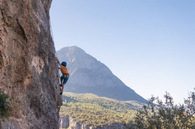 Çocuk kaya tırmanışçısı. Çocuk kayaya tırmandı. Çocuk doğal zeminde kaya tırmanışı yapmakla meşgul. Spor çocuğu aktif olarak zaman geçiriyor. Açık hava sporları yap.