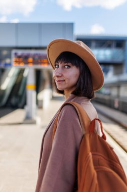 Trenle yolculuk. Paltolu ve şapkalı genç bir kadın istasyonda duruyor ve tren saatine bakıyor. macera ve seyahat.