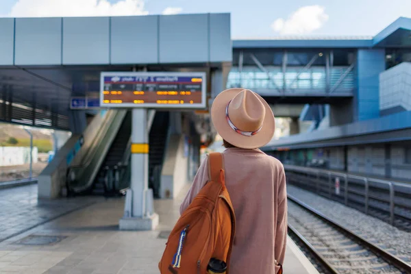 traveling by train. A young woman in a coat and hat stands at the station and looks at the train schedule. adventure and travel.
