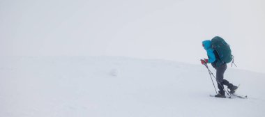 Dağlara tırmanan. Sırt çantalı ve kar ayakkabılı bir kız karda yürüyor. Dağlarda kış yürüyüşü.