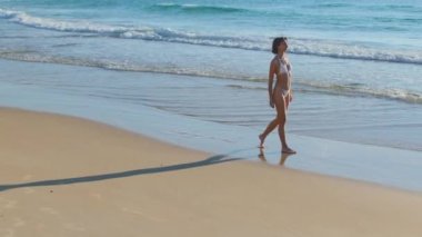 Mayolu genç bir kadın kumlu bir sahil boyunca yürüyor. Kız sahilde yavaşça yürüyor ve tatilin tadını çıkarıyor. Sahilde genç bir kızın silueti..