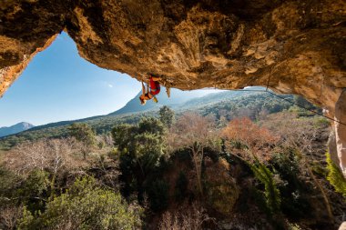 Kız kaya tırmanışçısı bir ormanın arka planına ve mavi dağlara tırmanır. Dağcı ekipman kullanarak zor bir yoldan geçiyor. Türkiye 'de kaya tırmanışı.