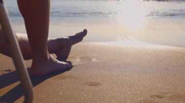 Yaz plajı tatili konsepti. Genç bir kız sahilde dinleniyor. Bir kız elinde şapkasıyla bir güneş pansiyonunda oturuyor. bacaklar kapalı.