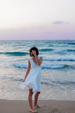 Beyaz bir yaz elbisesi içinde turkuaz denizli tropikal cennet plajının tadını çıkaran mutlu bir gezgin kız. Güzel beyaz elbiseli mutlu genç kadın gün batımında kumsalda yürüyor.. 