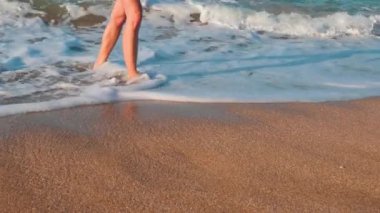 Genç bir kadın sudan çıkar ve kumlu sahil boyunca yürür. Kız sahilde yavaşça yürür ve tatilin tadını çıkarır. bacaklar kapalı..