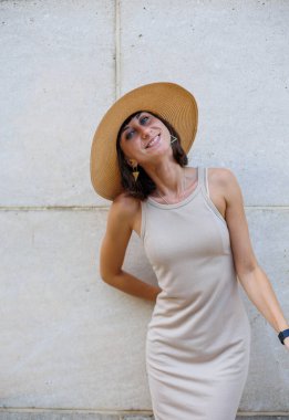 Moda bir yaz elbisesi içinde gülümseyen güzel bir kız. Sokakta şapkalı, duvara karşı poz veren seksi kaygısız kadın. Eğlence ve kahkaha.